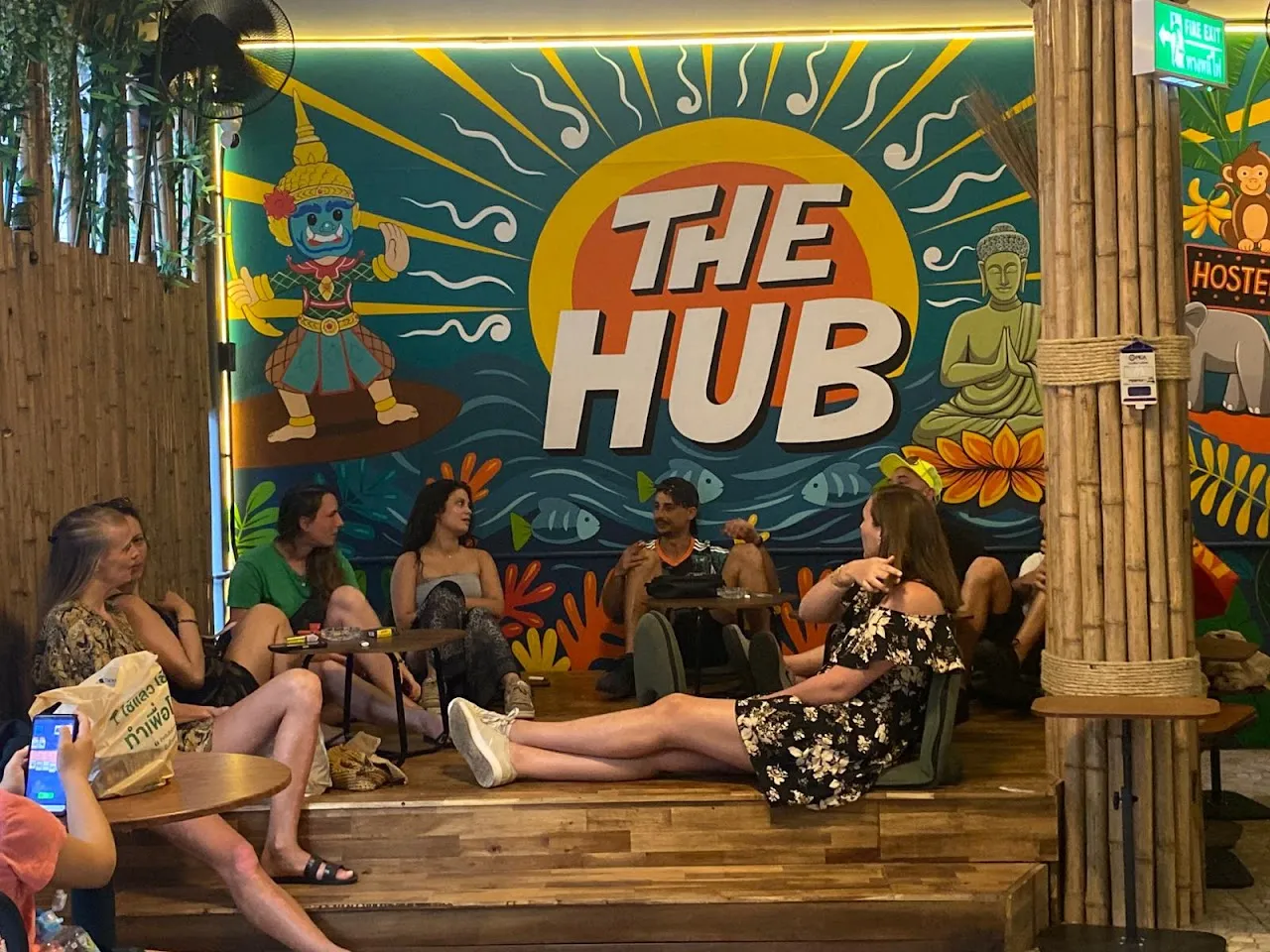 Guests relaxing in The Hub's tropical bamboo lounge under the hand-painted mural in Ao Nang